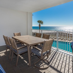 Enjoy dining on the spacious balcony with a stunning beachfront view, featuring a wooden table and comfortable seating