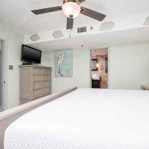 The comfortable bedroom features a light green wall, a king bed, a TV mounted above a dresser, and an adjoining bathroom
