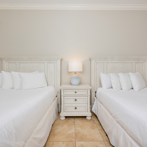 Bright and airy guest bedroom featuring two cozy queen beds, a stylish nightstand, and soft white linens for a restful stay
