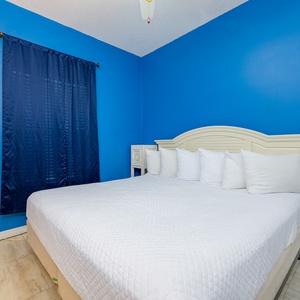 The master bedroom features a bright blue accent wall, a king bed with plush pillows, and a cozy atmosphere for relaxation