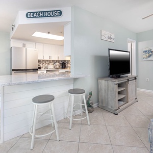 The inviting living area features a comfortable sofa, a TV on a rustic stand, and a breakfast bar with stylish seating