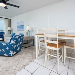 The living area features blue starfish-patterned chairs, a cozy sofa, and a stunning beachfront view through large windows