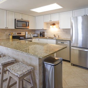 Modern kitchen features a spacious granite countertop with seating, stainless appliances, and warm lighting