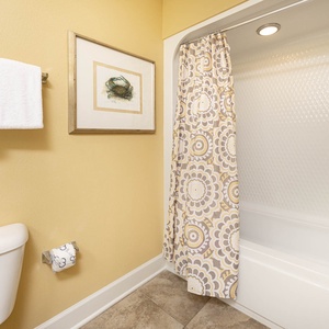 Bright yellow walls and floral shower curtain enhance this cozy guest bathroom featuring a tub/shower combo and fresh towels