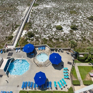The pool area features a large swimming pool, kiddie pools, and shaded seating under blue umbrellas
