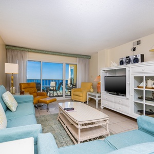 The living area features light blue and yellow decor, a TV, and a stunning beachfront view from the balcony