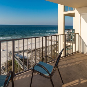 The balcony features a chair overlooking the white sand beach and tranquil waves, creating a serene coastal retreat