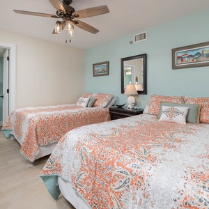 Two brightly colored queen beds in this inviting geust room, complemented by a ceiling fan and soft aqua walls