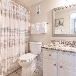 This bathroom features a stylish granite countertop, a large mirror, and a relaxing shower with a striped curtain