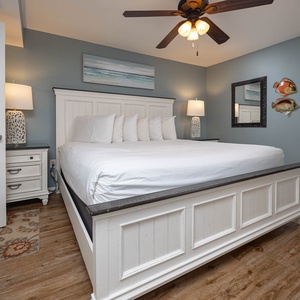 Cozy bedroom featuring a king bed with white linens, decorative fish art, and a stylish lamp beside a mirrored wall