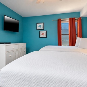 This guest bedroom features two comfortable full beds, a wall-mounted TV, and vibrant orange curtains against a teal backdrop