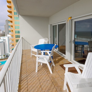 Enjoy stunning beachfront views from this balcony, featuring a blue table and white chairs for relaxing moments