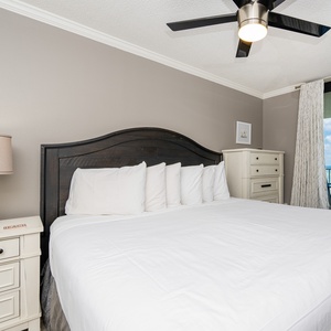 Cozy master bedroom features a large king bed with white linens, a stylish nightstand, and balcony access on the beach
