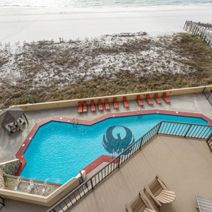 Balcony view from above showcasing the vibrant pool area with red lounge chairs and a path leading to the beach front beyond