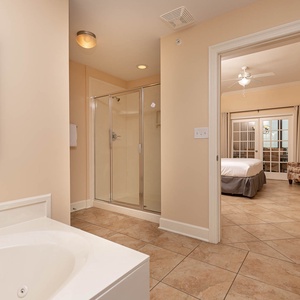 The master bath features a relaxing jetted tub and a glass walk-in shower, leading to a cozy bedroom with a charming view