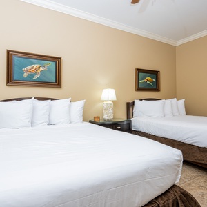 This guest bedroom features two comfortable queen beds, charming turtle artwork, and a bedside lamp for a cozy ambiance