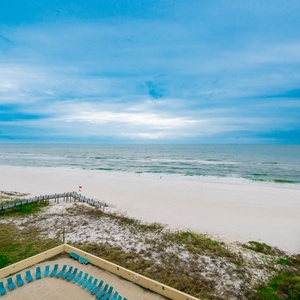 Stunning view of the serene beach and gentle waves from a cozy balcony with turquoise lounge chairs below