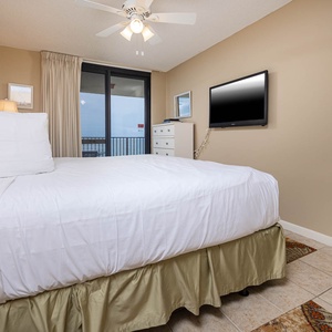 Inviting master bedroom featuring a plush king bed, a wall-mounted TV, and access to a balcony with views of the gulf
