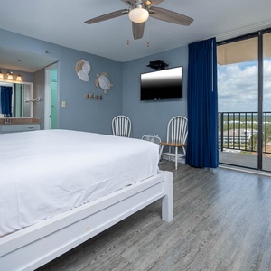The master bedroom features a comfortable king bed, a wall-mounted TV, and a beautiful view from the balcony
