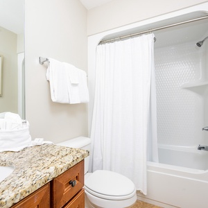 This bathroom features a stylish granite countertop, a relaxing tub shower combo, and fresh white towels for your comfort