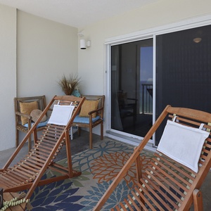 Relax on the wooden loungers on this balcony, enjoying the vibrant rug and the inviting view of the beachfront