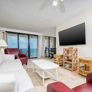 This living area features a large TV, cozy white and red seating, queen sofa-sleeper, and a beautiful view of the beach