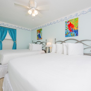 Brightly decorated guest bedroom featuring two queen beds, colorful artwork, and blue curtains for a vibrant atmosphere