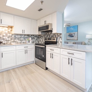 Modern kitchen featuring sleek white cabinetry, a stylish hexagonal backsplash, stainless appliances, and a beachfront view