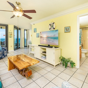 The inviting living room features blue furnishings, a large TV, and a tropical plant, creating a relaxed beach vibe