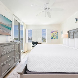 A restful master suite features a king bed and views of shimmering water beyond shuttered windows and glass doors