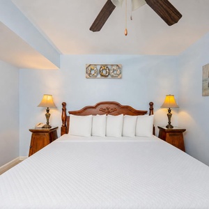 Cozy king suite with fluffy pillows framed by calm coastal art and soft glowing lamps at night
