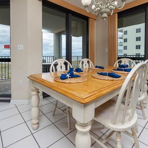 Dining area features a wooden table set for six with blue napkins, adjacent to sliding glass doors leading to a balcony