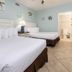 Relax in this inviting guest room featuring two comfortable double beds, coastal decor, and a bright, airy atmosphere