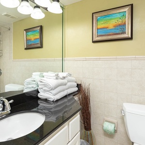 The guest bathroom features a sleek black countertop with a round sink, neatly stacked towels, and a colorful artwork above