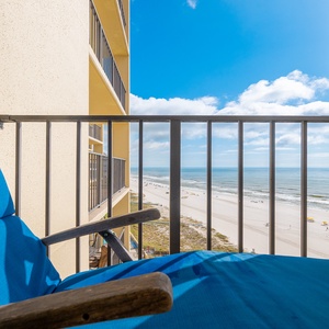 A vibrant blue chair on the balcony offers a clear view of the beach and gentle waves under a bright sky