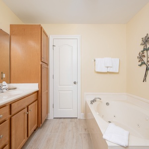 Master bathroom featuring a jetted tub, walk-in shower, warm wood cabinetry, and elegant floral wall decor