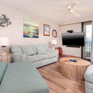 Living room featuring soft teal sofas with a queen sleeper, a wooden coffee table, and a large TV