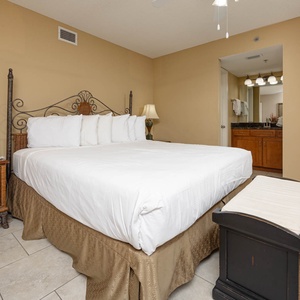 Master suite with a king bed, wicker nightstand, and a view into the master bath featuring a stylish vanity