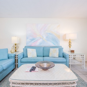 This inviting living area features soft blue seating, a TV, and a view of the kitchen, perfect for relaxation and gatherings