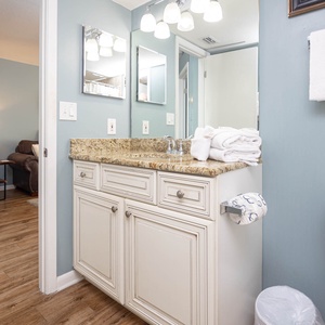 Bathroom featuring a granite countertop with neatly stacked towels, a stylish sink, and a glimpse of a cozy living area