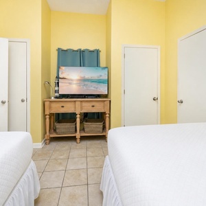 Cozy guest bedroom with two queen beds and a TV on a wooden stand, creating a cheerful and inviting atmosphere