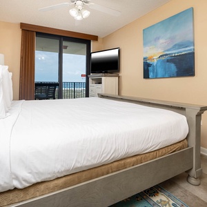 Cozy master bedroom features a king bed, a flat-screen TV, and balcony access with views of the beach and gulf beyond