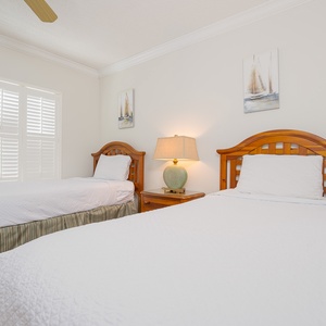 Two twin beds in this guest room are set against a textured green wall, complemented by a cozy area rug and bedside lamp