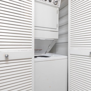 Convenient laundry area featuring a stacked washer and dryer behind stylish white louvered doors for easy access