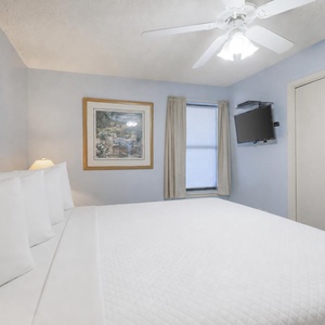 Brightly colored walls complement the spacious bedroom featuring a king bed, a TV, and natural light from the window