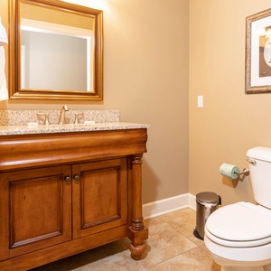 This half bath features elegant wooden cabinetry, a granite countertop, and a stylish mirror for a refined touch