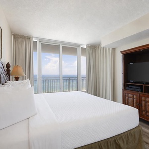 The master bedroom features a plush bed, elegant decor, and a stunning beach view, complemented by a TV for entertainment