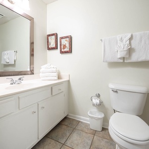 Bright guest bathroom featuring a large mirror, white cabinetry, neatly stacked towels, and decorative artwork on the wall