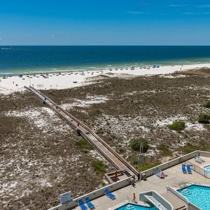 View of the beach with white sand, lounge chairs, and a wooden walkway leading to the water, alongside the pool area