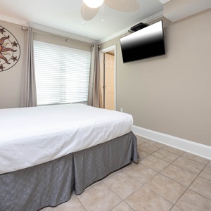 This cozy bedroom features a comfortable bed, a TV for entertainment, and a charming sun-themed wall decor